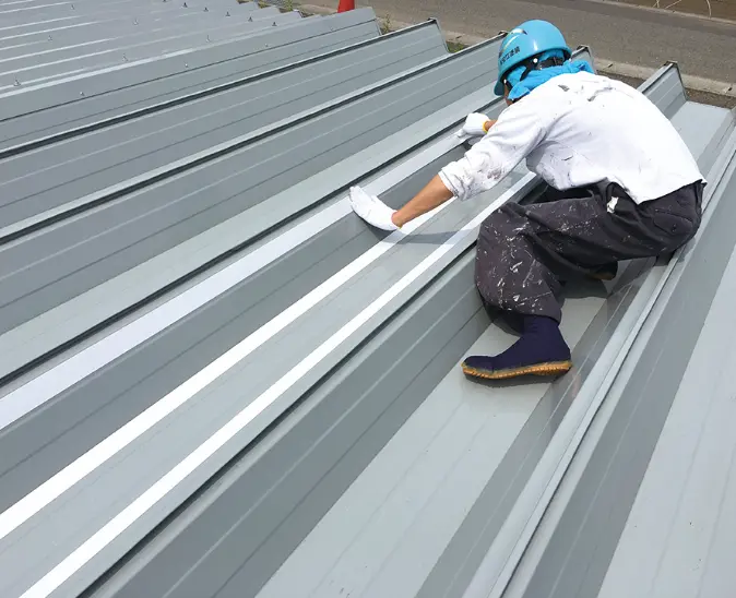 折板屋根の上にしゃがみ込み丁寧な施工・現地調査を行う作業員